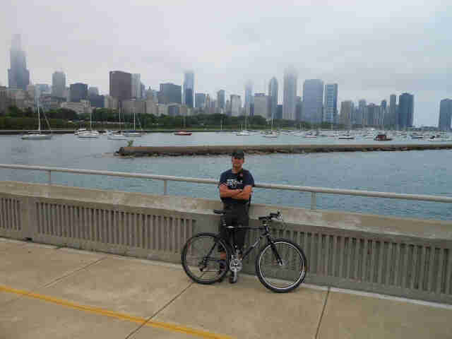 Right side view of a black Surly bike leaning on the cyclist behind, on a bridge with a bay and city, in the background
